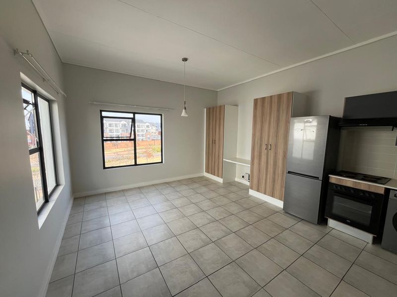 An open-plan living and kitchen area featuring tiled floors, built-in cabinetry, and integrated kitchen appliances in a clean, modern apartment setting.