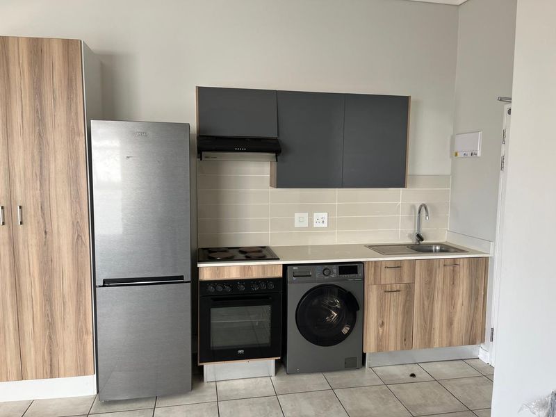 Compact modern kitchen featuring wood-grain cabinetry, integrated oven and hob, extractor fan, and tiled backsplash with a functional sink area.