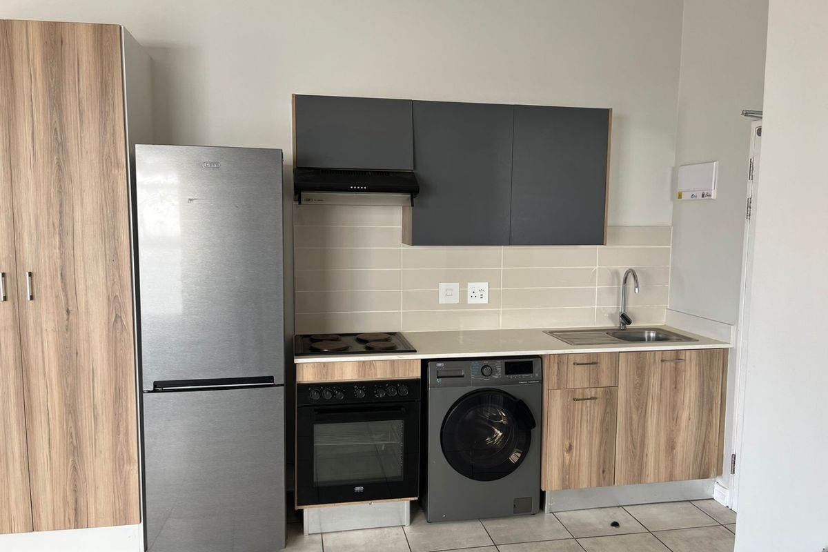 Modern kitchen featuring wood-look cabinetry, grey upper cupboards, integrated electric oven and hob, extractor fan, and tiled backsplash.