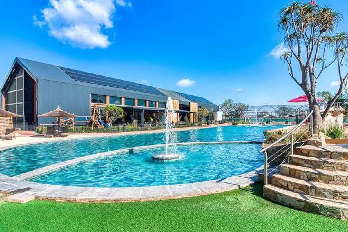 A well-maintained communal swimming pool area featuring a central water fountain, stone steps with stainless steel railings, and a modern building with solar panels.