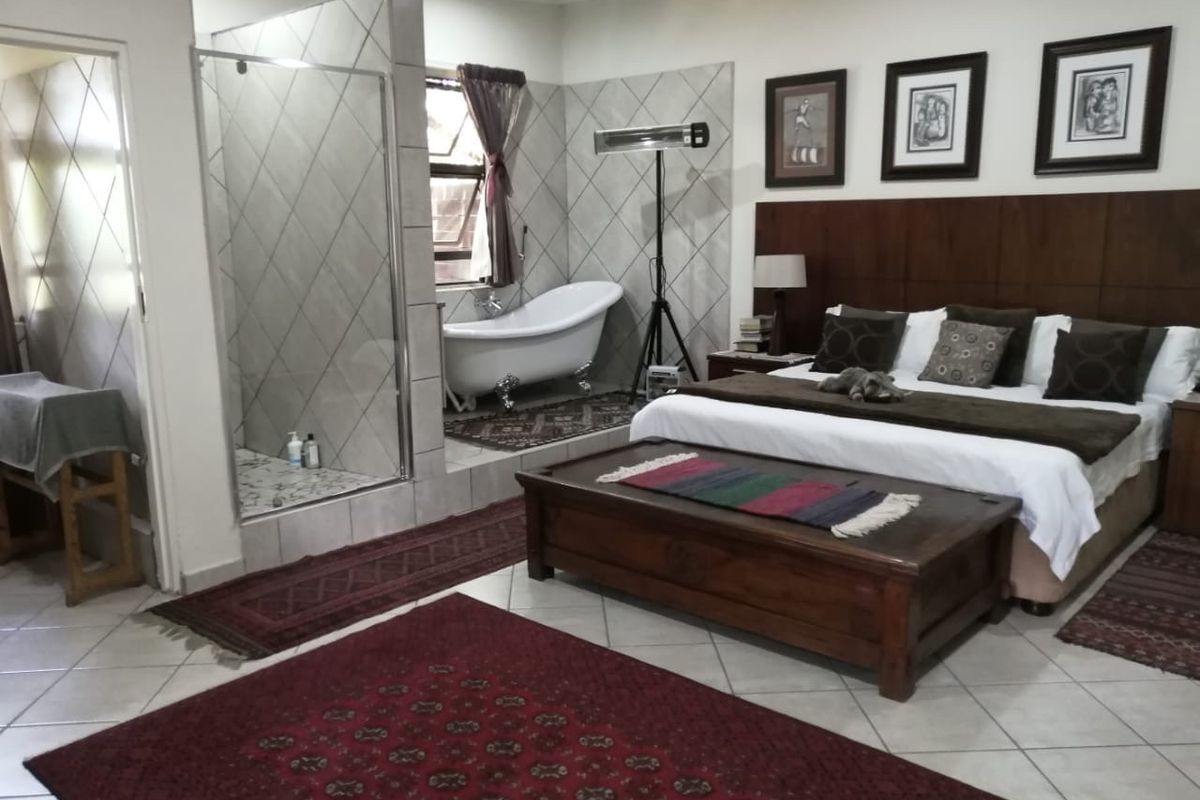 Spacious bedroom featuring an open-plan en-suite area with a freestanding bathtub and a glass-enclosed shower, complemented by tiled flooring and a built-in headboard.