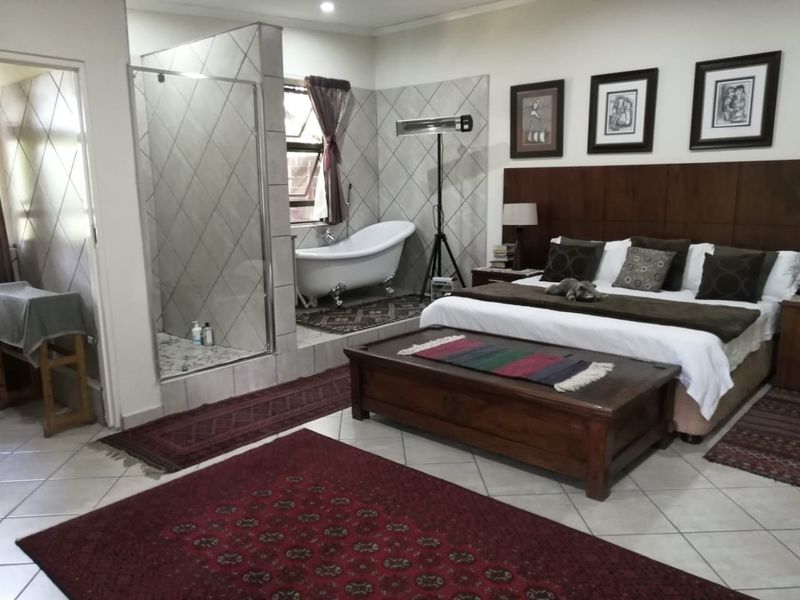 Spacious bedroom featuring an open-plan en-suite area with a freestanding bathtub and a glass-enclosed shower, complemented by tiled flooring and a built-in headboard.
