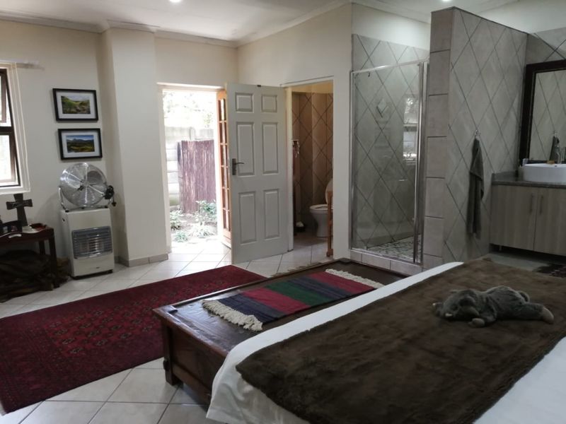 Spacious bedroom featuring an open-plan en-suite bathroom with a glass shower, vanity, and direct access to an outdoor area.