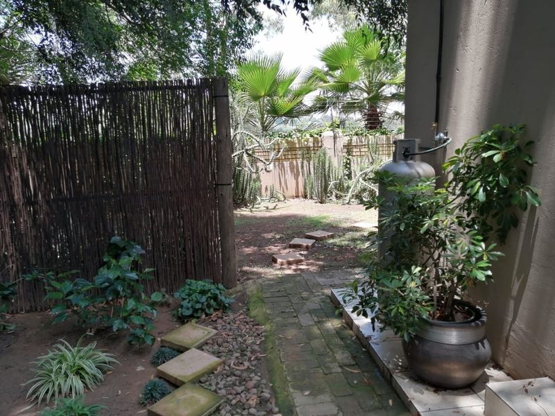 A private garden area featuring a brick pathway, reed screen fencing, and a gas cylinder installation against the exterior wall.