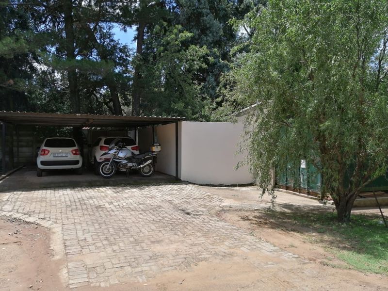 Outdoor carport area with paved driveway and boundary wall, providing covered parking space for vehicles.