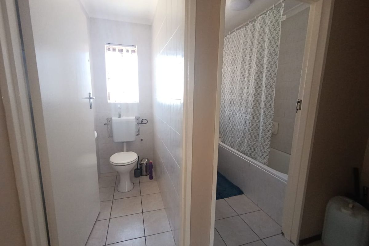 A functional bathroom featuring a separate toilet area and a bathtub with shower facilities, finished with ceramic tiling throughout.