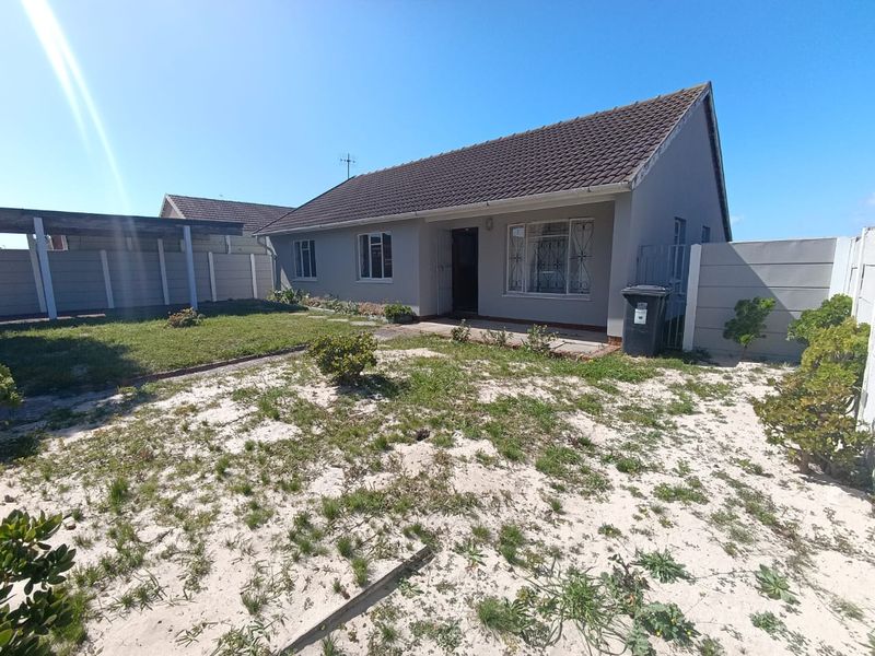 Rear view of a detached house featuring a tiled roof, security bars on windows, a carport, and a large garden area with sandy soil.