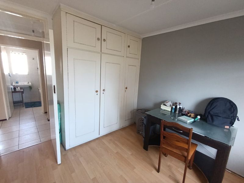 Bedroom featuring built-in wardrobes and laminate flooring, with an adjacent view into a tiled bathroom area.