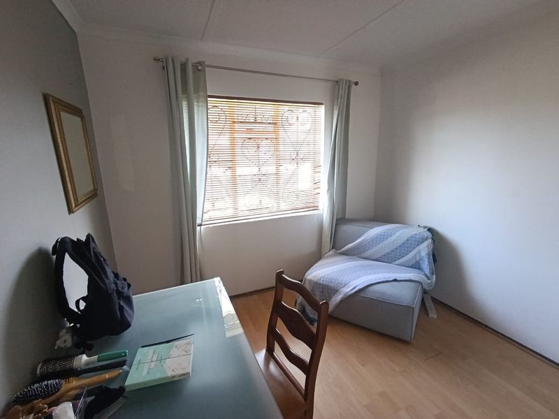 A bedroom featuring laminate flooring and a window fitted with security bars.