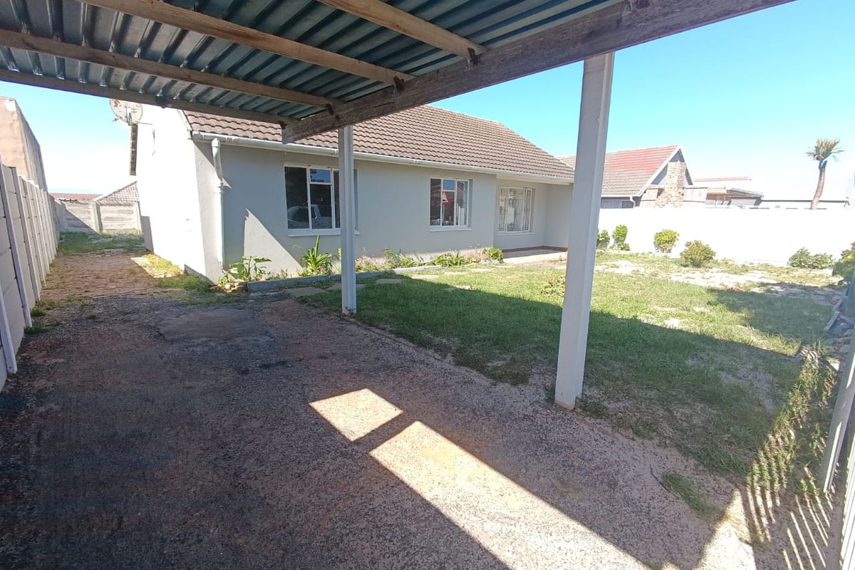 Rear view of the property featuring a covered carport, concrete driveway, and a private garden area enclosed by perimeter boundary walls.
