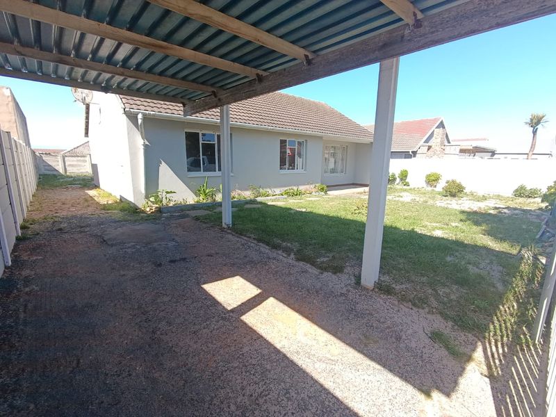 Rear view of the property featuring a covered carport, concrete driveway, and a private garden area enclosed by perimeter boundary walls.