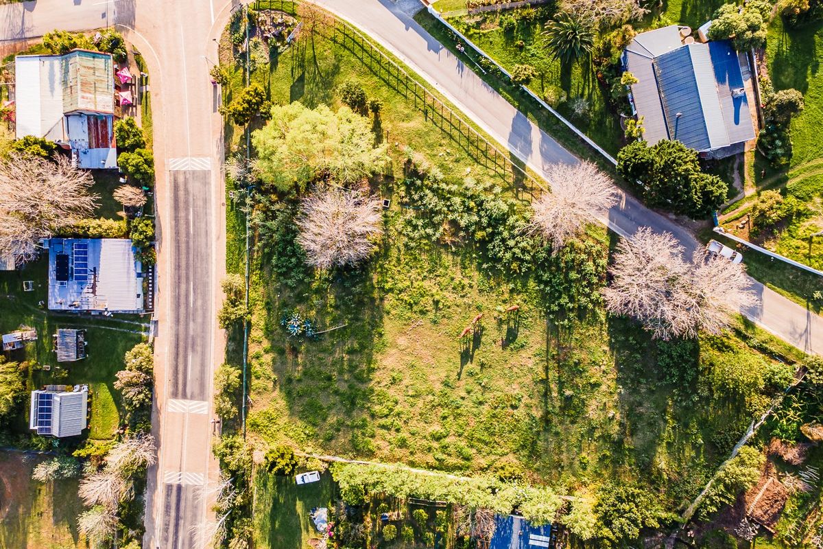 Aerial view of a vacant residential plot situated on a corner lot, featuring established trees and perimeter fencing in a suburban neighborhood.