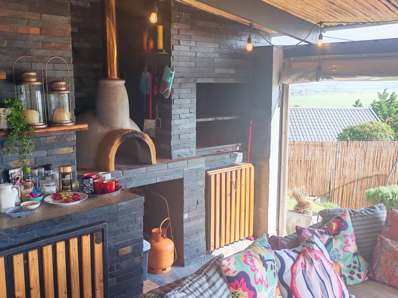 Covered outdoor entertainment area featuring a built-in pizza oven, braai, and stone-clad finishes, offering a functional space for alfresco dining and relaxation.