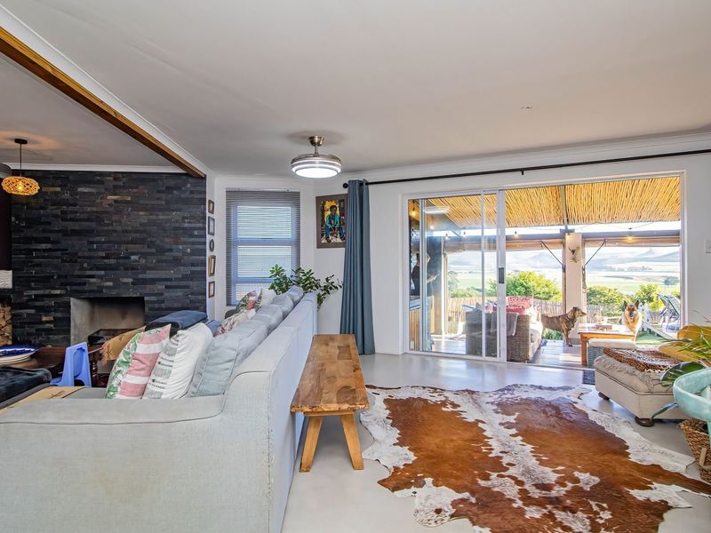 Spacious living room featuring a striking stone-clad fireplace, polished concrete floors, and large sliding glass doors that open onto a covered patio with scenic views.