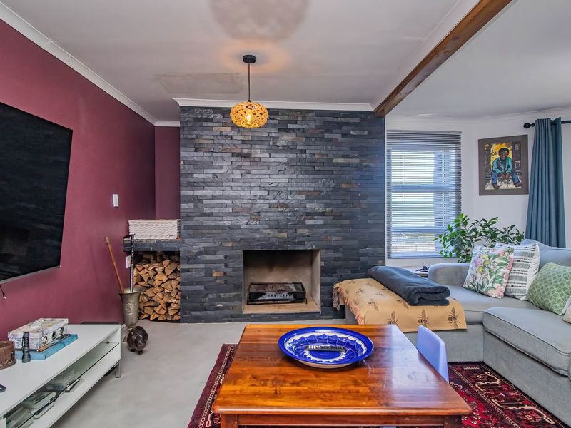 Living room featuring a prominent stone-clad fireplace with integrated log storage, polished concrete flooring, and a ceiling fan.