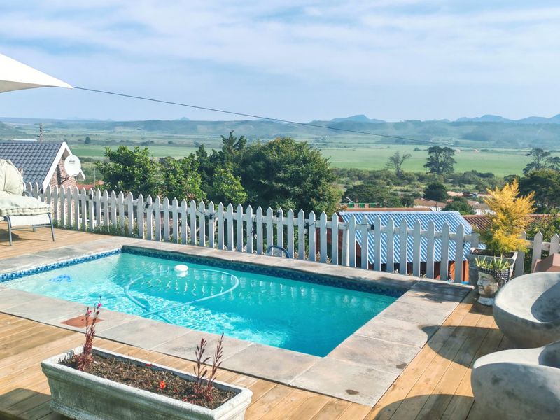 Outdoor pool area featuring timber decking, stone coping, and a picket fence, offering expansive scenic views of the surrounding landscape.