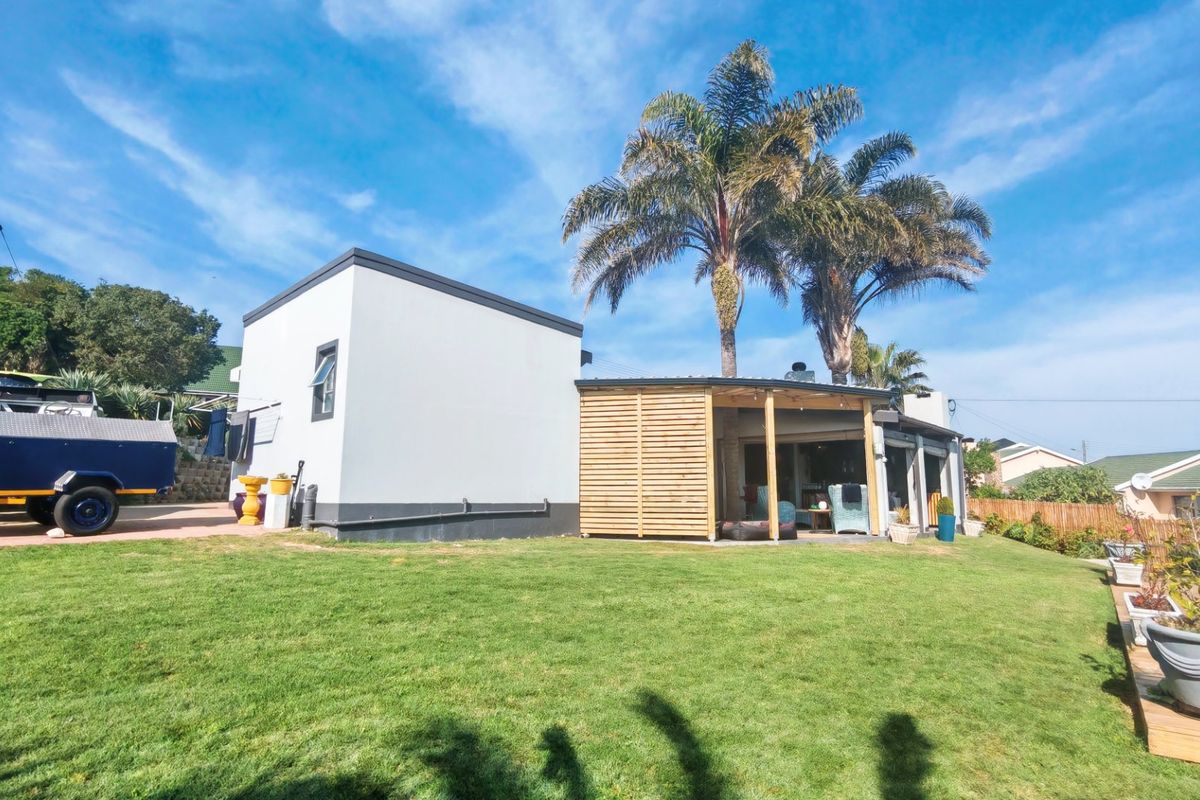 Rear view of the property featuring a well-maintained lawn, a covered patio area with timber slat screening, and mature palm trees.
