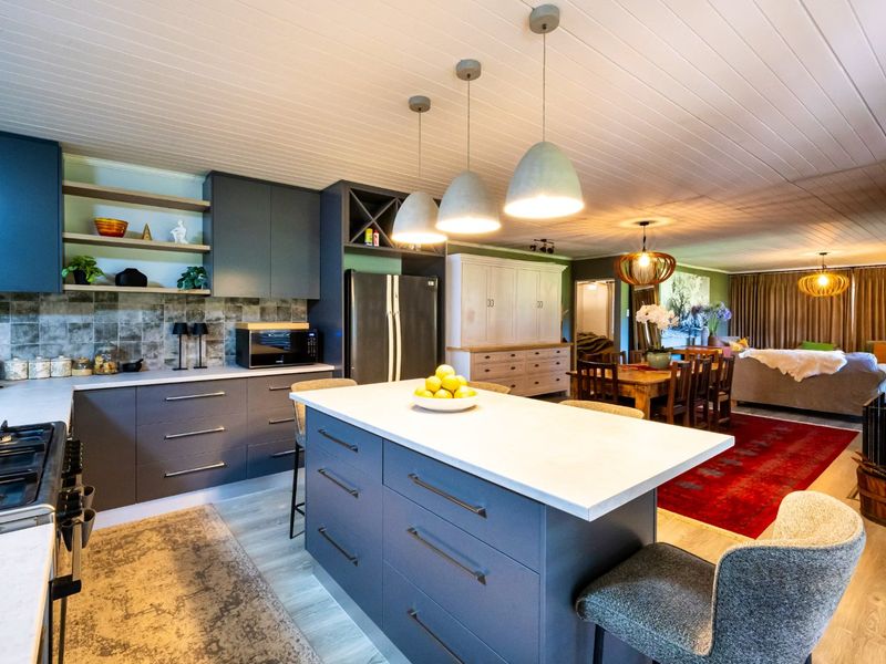 Spacious open-plan kitchen and living area featuring a central island, modern cabinetry, gas cooktop, and stylish pendant lighting under a timber-paneled ceiling.