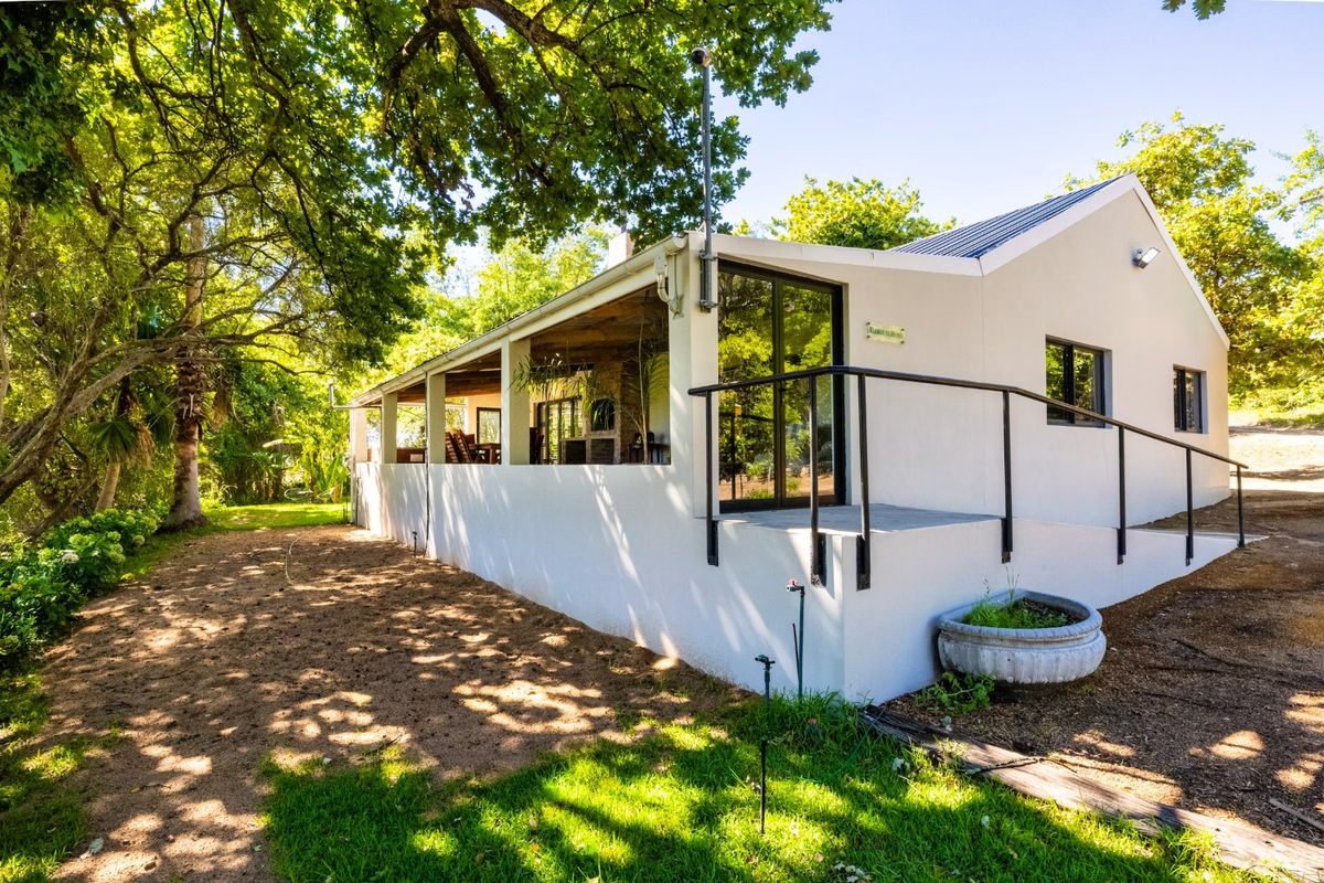 A well-maintained rear exterior view of the house featuring a covered patio, concrete ramp access, and large sliding glass doors set in a garden.