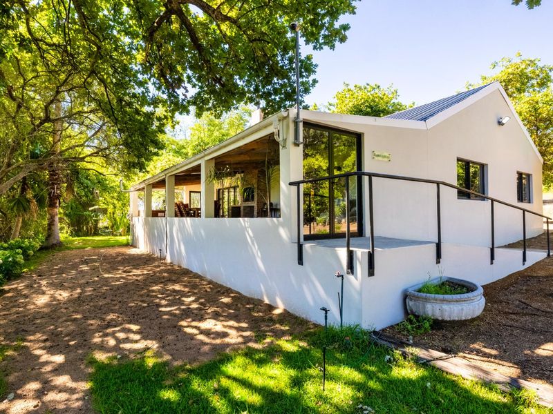 A well-maintained rear exterior view of the house featuring a covered patio, concrete ramp access, and large sliding glass doors set in a garden.