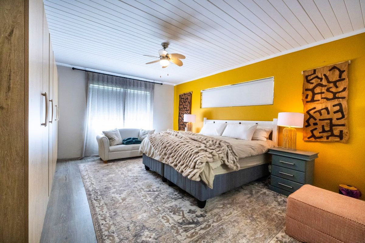 Spacious bedroom featuring built-in cupboards, a ceiling fan, and modern laminate flooring with a bright accent wall.