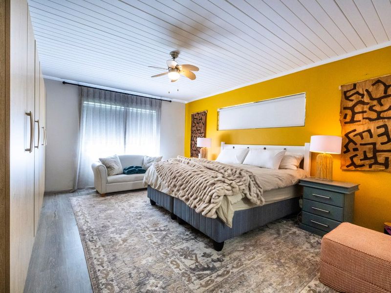 Spacious bedroom featuring built-in cupboards, a ceiling fan, and modern laminate flooring with a bright accent wall.
