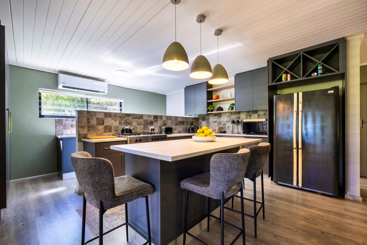 Modern kitchen featuring a central island, dark cabinetry, tiled splashback, and integrated appliances, complemented by contemporary pendant lighting and timber-look flooring.