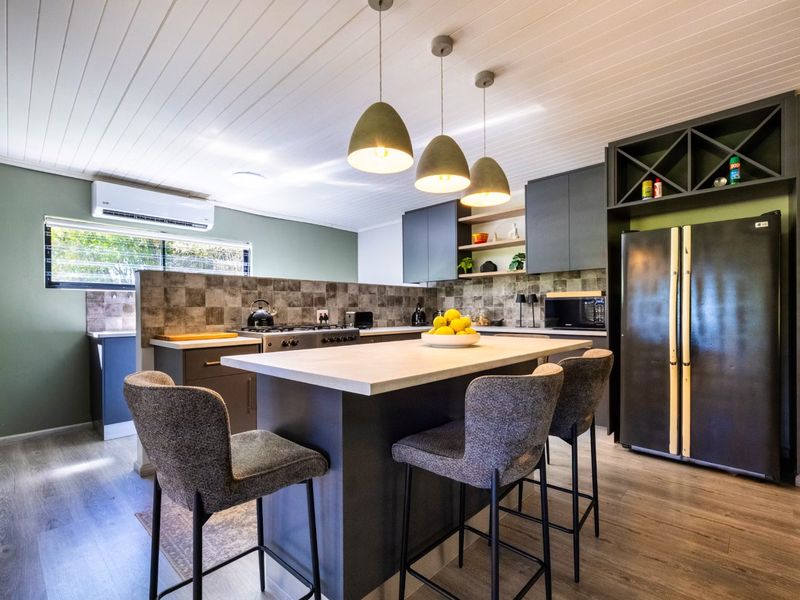 Modern kitchen featuring a central island, dark cabinetry, tiled splashback, and integrated appliances, complemented by contemporary pendant lighting and timber-look flooring.