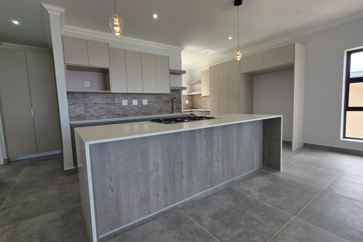 Modern kitchen featuring a central island with a gas hob, stone countertops, neutral cabinetry, and large format floor tiles in an open-plan layout.