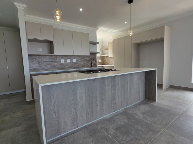 Modern kitchen featuring a central island with a gas hob, stone countertops, neutral cabinetry, and large format floor tiles in an open-plan layout.