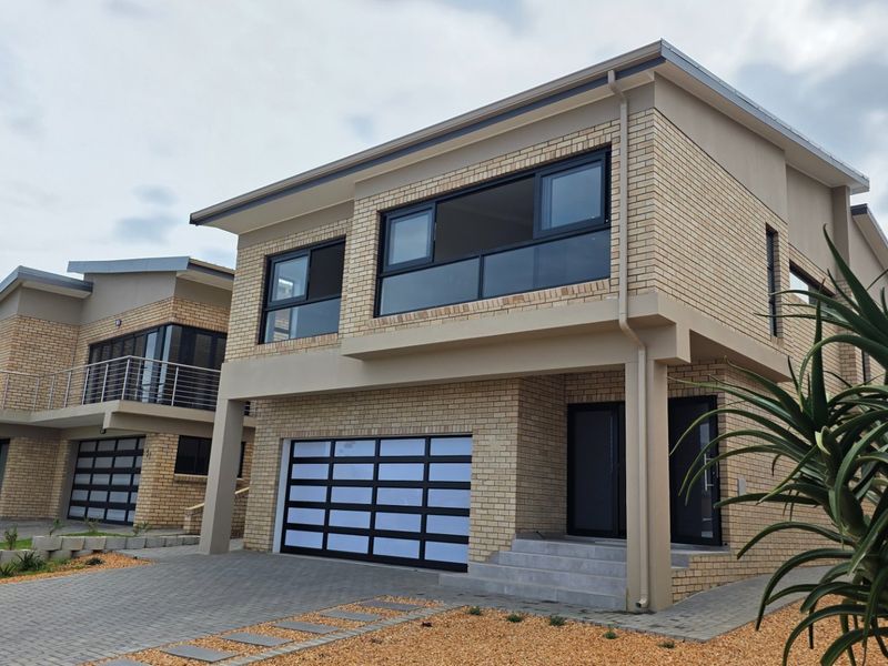 Modern double-storey brick house featuring a paved driveway, integrated garage, and upper-level balcony with contemporary aluminium window frames.