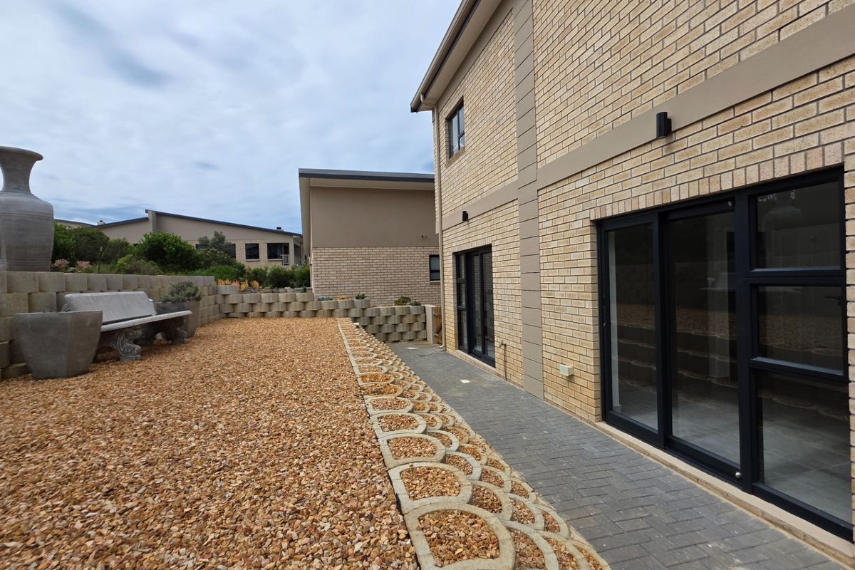Rear exterior view of the house featuring a brick facade, sliding glass doors, a paved walkway, and a landscaped gravel garden area.