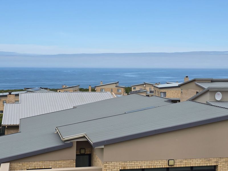 Elevated view overlooking a residential estate with modern corrugated metal roofs and a scenic ocean horizon in the background.