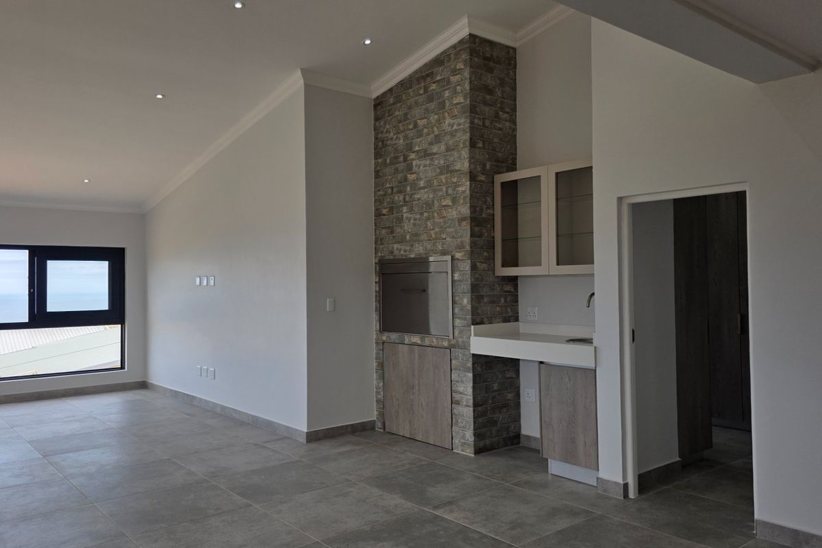 Spacious living area featuring a built-in braai with stone cladding, modern tiled flooring, recessed lighting, and a convenient built-in kitchenette area.