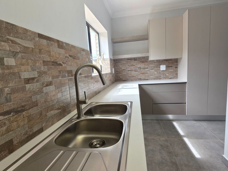 A modern, clean scullery featuring a double bowl stainless steel sink, stone countertops, stacked stone backsplash, and ample built-in cabinetry.