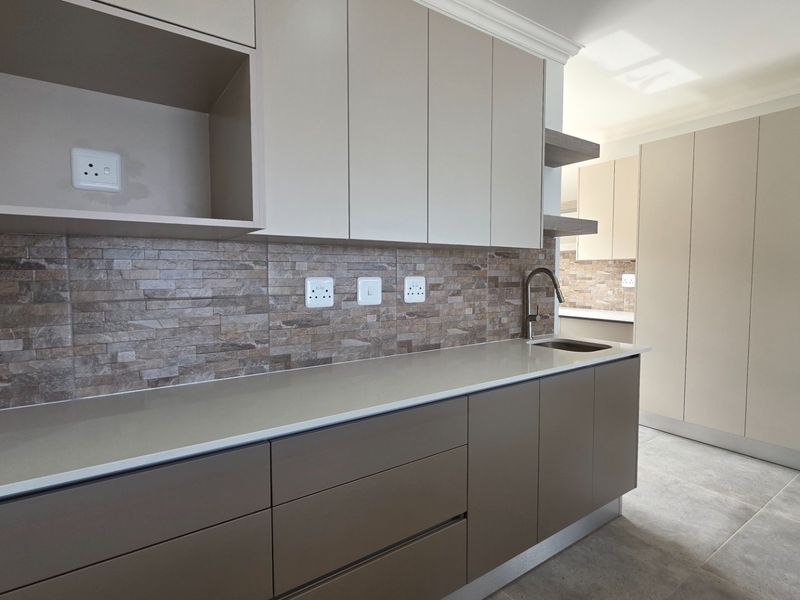Modern kitchen featuring neutral-toned cabinetry, stone-look tile backsplash, quartz countertops, and an undermount sink with a contemporary gooseneck faucet.