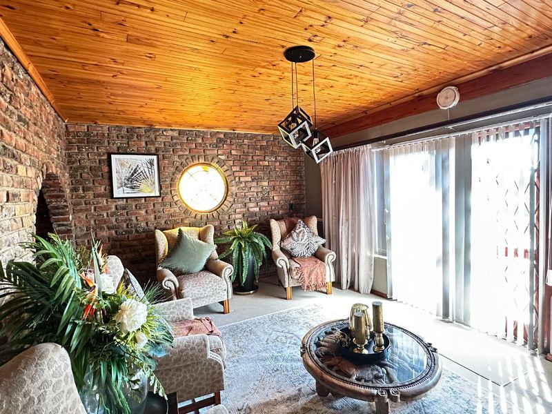 A cozy living room featuring an exposed brick wall, a distinctive porthole window, and a warm timber-paneled ceiling with sliding doors leading outdoors.