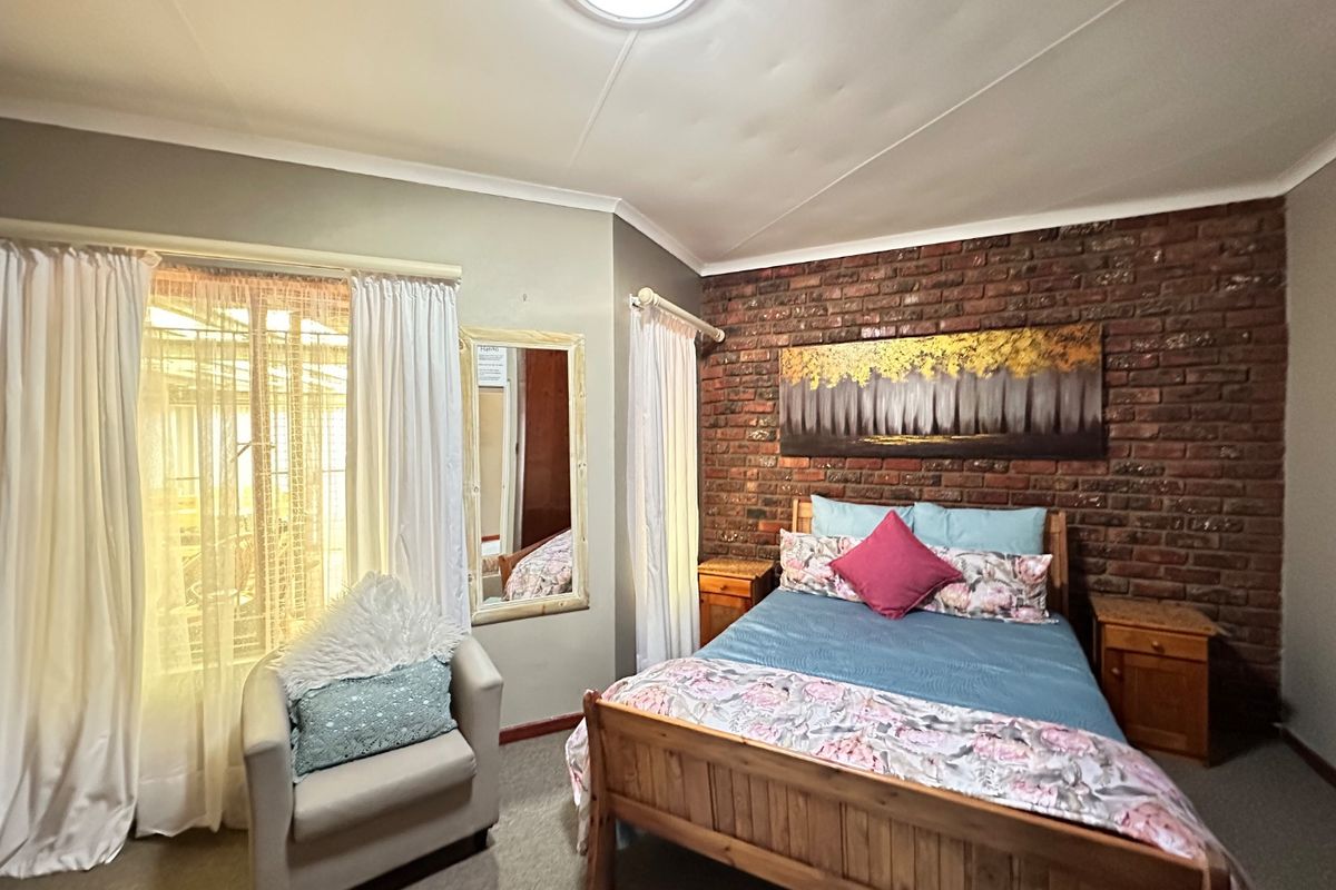 A bedroom featuring an exposed brick accent wall, neutral wall finishes, and natural light through a large window with curtain fixtures.