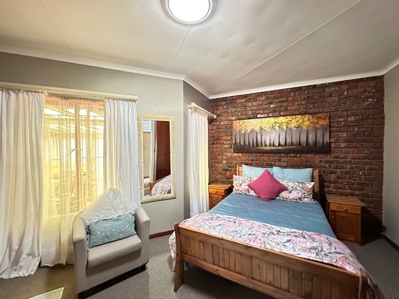 A bedroom featuring an exposed brick accent wall, neutral wall finishes, and natural light through a large window with curtain fixtures.