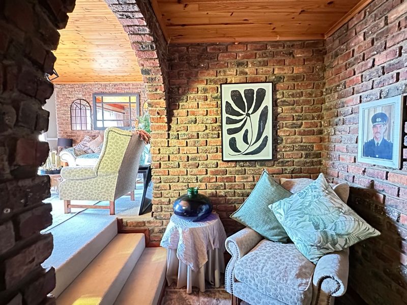 A cozy living area featuring rustic exposed brick walls, a warm timber-clad ceiling, and a distinctive brick archway leading to an adjacent space.
