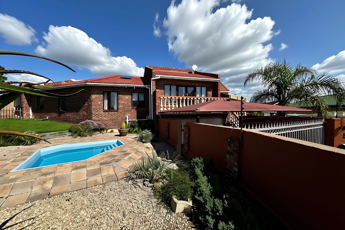 Rear view of a brick house featuring a swimming pool, paved surround, and an upper-level balcony with a balustrade.