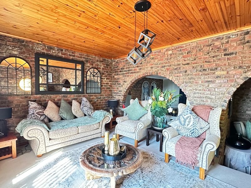 A cozy living room featuring rustic exposed brick walls, a warm timber ceiling, and a distinctive brick archway.