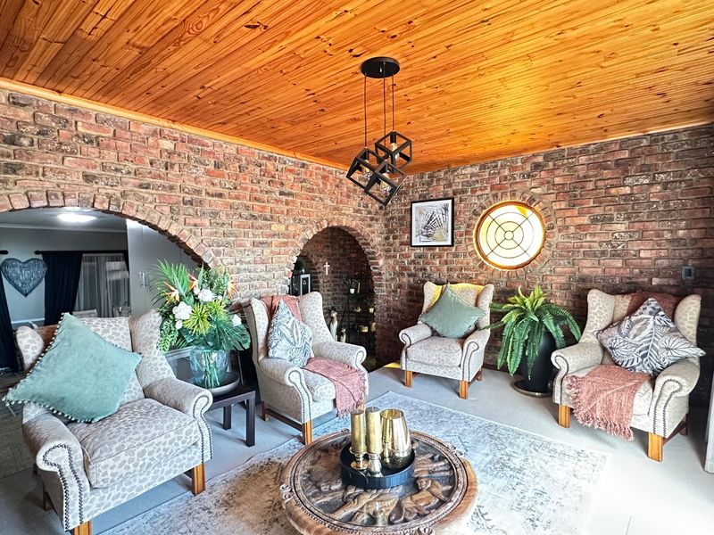 A characterful living room featuring exposed brick walls, a warm timber ceiling, and unique arched architectural details with a circular feature window.