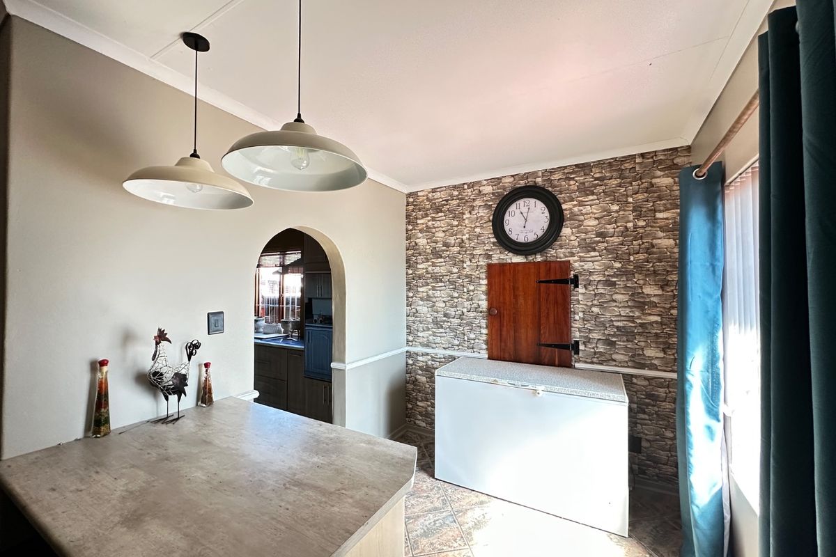 A kitchen area featuring a stone-effect feature wall, arched doorway leading to a secondary space, pendant lighting, and tiled flooring.