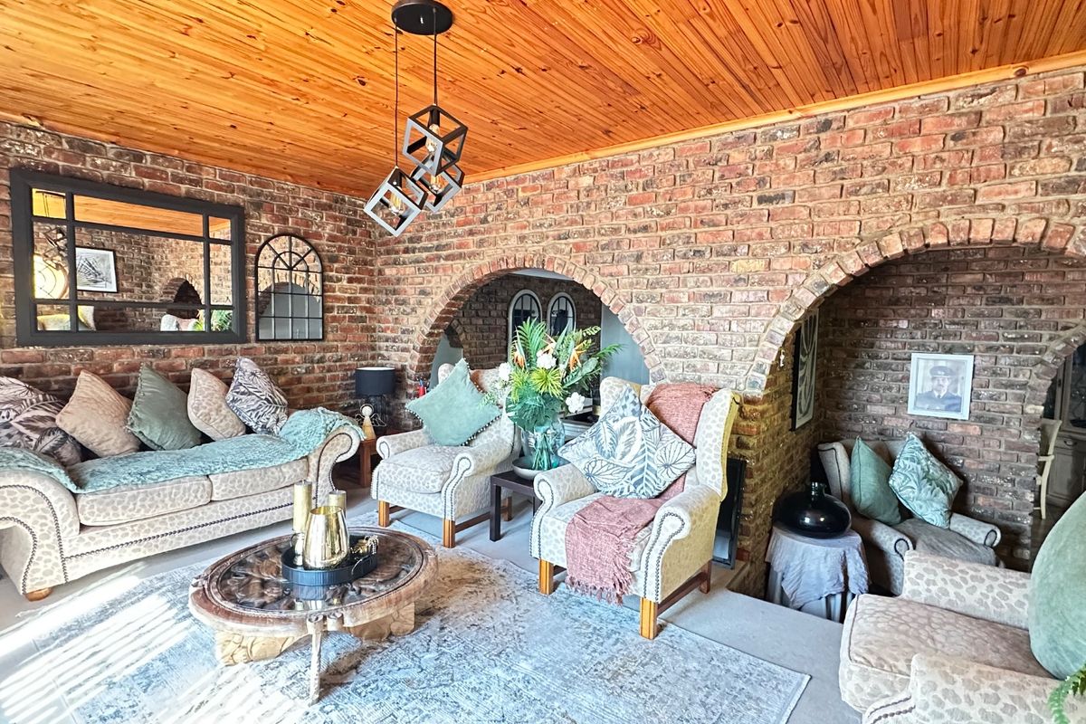 A rustic living room featuring exposed brick walls, distinctive brick archways, and a warm timber tongue and groove ceiling with a sunken floor area.