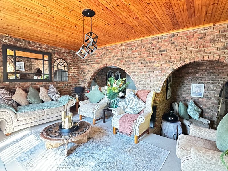 A rustic living room featuring exposed brick walls, distinctive brick archways, and a warm timber tongue and groove ceiling with a sunken floor area.