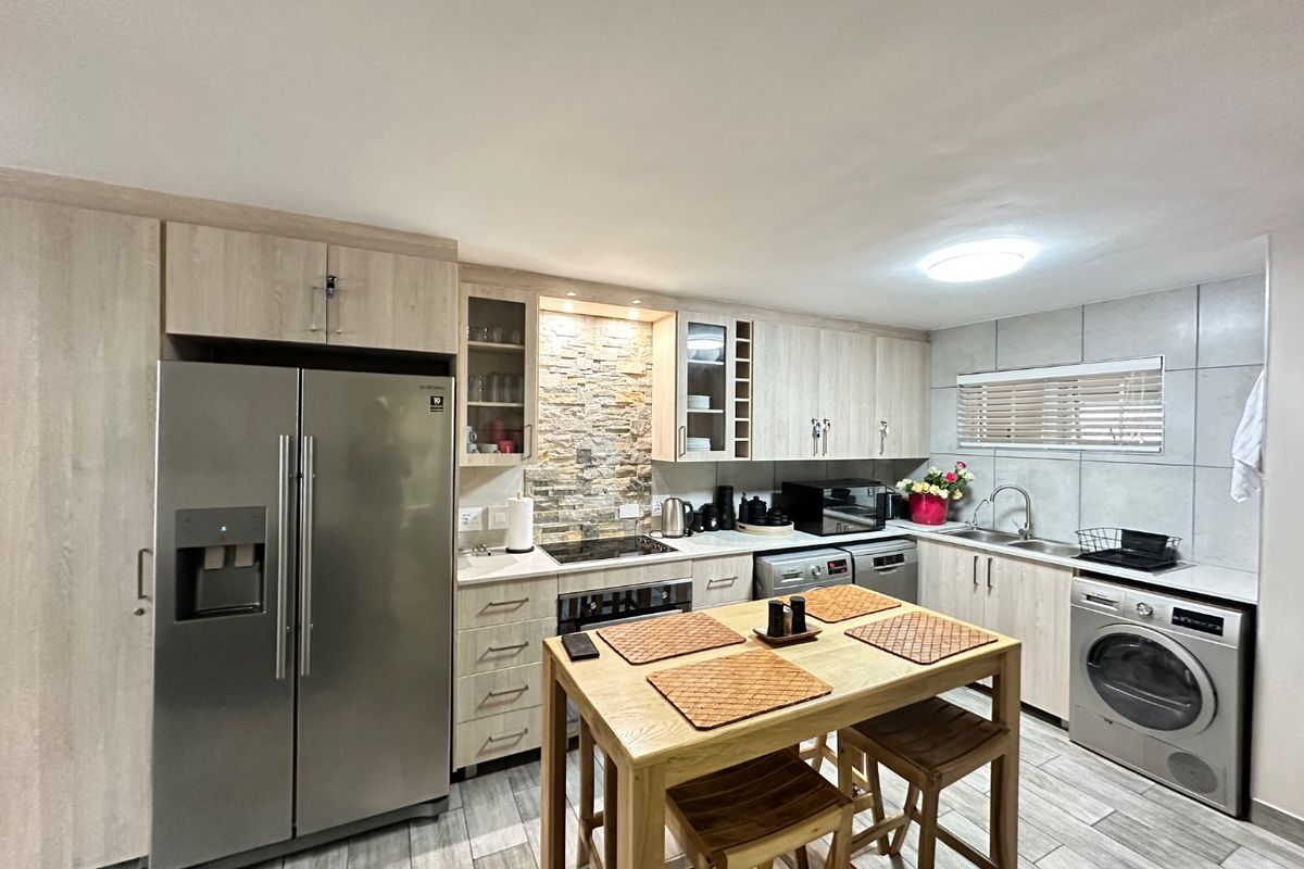 Modern kitchen featuring light wood cabinetry, stone veneer backsplash, stainless steel appliances, and tiled flooring with a central dining island.
