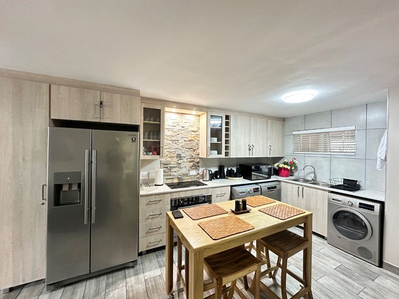 Modern kitchen featuring light wood cabinetry, stone veneer backsplash, stainless steel appliances, and tiled flooring with a central dining island.