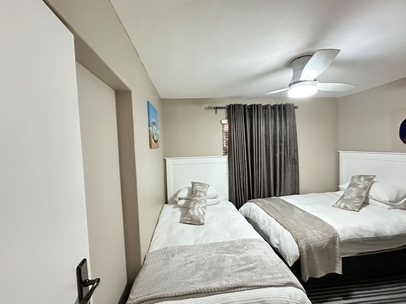 A well-maintained bedroom featuring a ceiling fan, neutral wall tones, and built-in headboards, providing a comfortable and functional sleeping space.