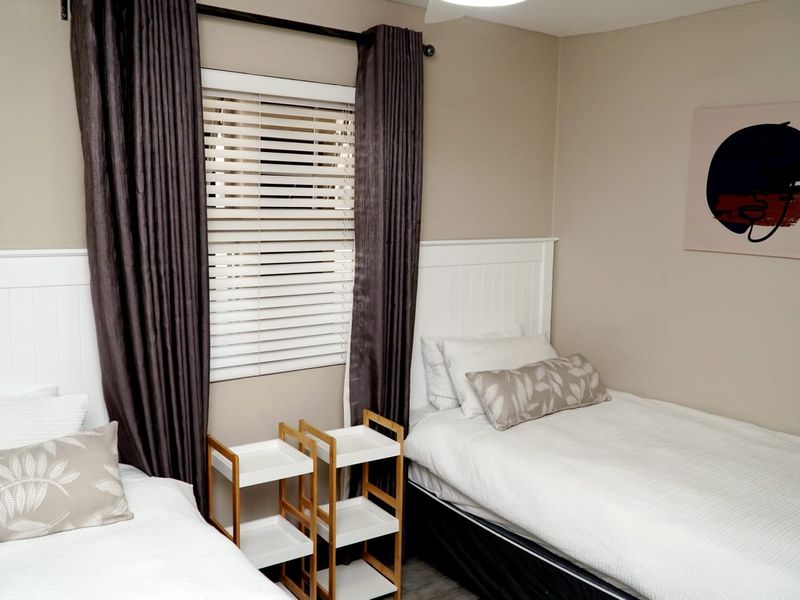 A well-maintained bedroom featuring neutral wall tones, beadboard headboards, and venetian blinds with dark curtains.